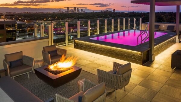 Rooftop patio with comfortable chairs, fire pit, and pool with purple lights.